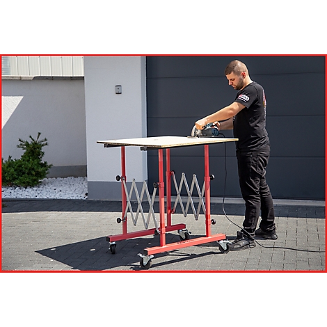 Mann schneidet mit Kreissäge Holzplatte auf rotem, höhenverstellbarem Arbeitstisch.